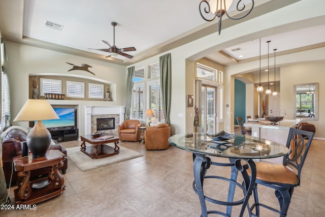 living room with a tray ceiling, a fireplace, light tile patterned floors, visible vents, and ceiling fan with notable chandelier