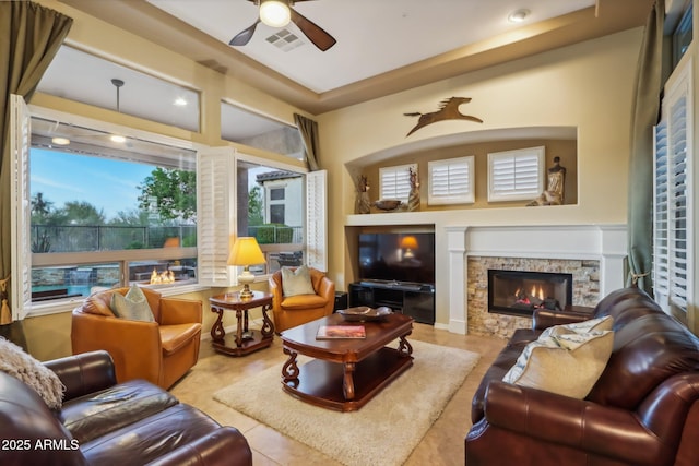 living room featuring ceiling fan, a fireplace, and light tile patterned floors