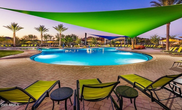 pool at dusk featuring a patio and a community pool