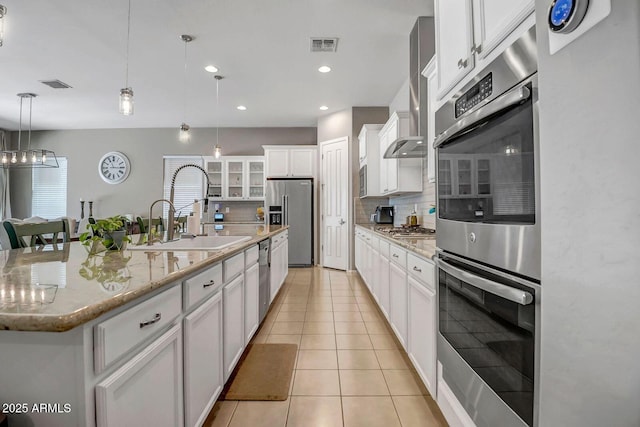 kitchen with a center island with sink, sink, hanging light fixtures, appliances with stainless steel finishes, and white cabinets