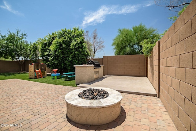 view of patio / terrace featuring a playground, an outdoor kitchen, and an outdoor fire pit