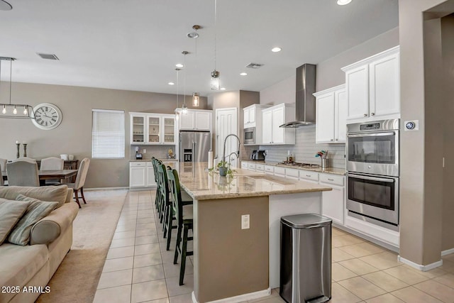 kitchen with decorative light fixtures, appliances with stainless steel finishes, wall chimney range hood, and a center island with sink