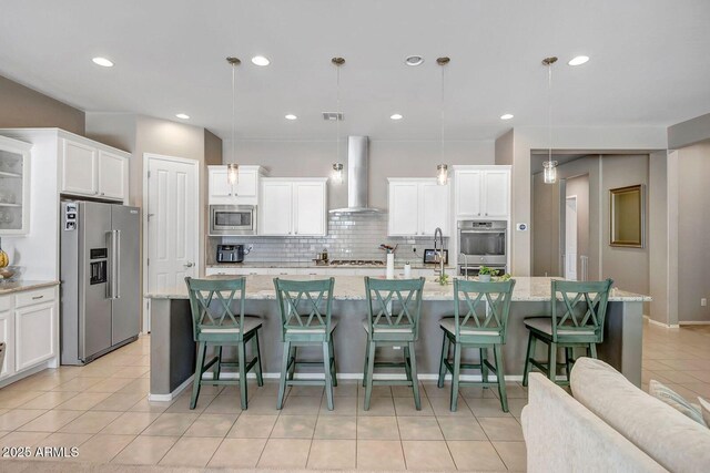 kitchen featuring hanging light fixtures, a center island with sink, stainless steel appliances, and wall chimney exhaust hood