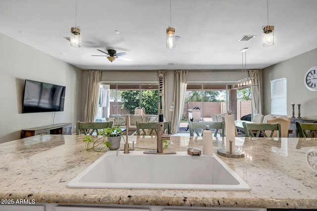 kitchen with decorative light fixtures, light stone countertops, and ceiling fan