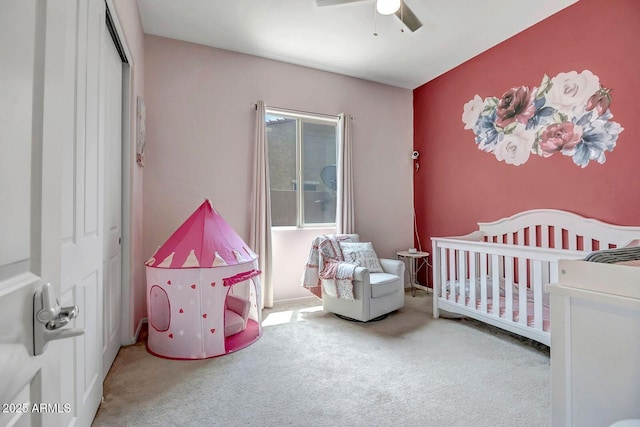 carpeted bedroom with ceiling fan, a nursery area, and a closet