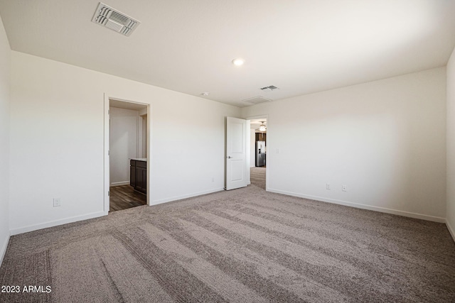 unfurnished bedroom featuring carpet floors, freestanding refrigerator, visible vents, and baseboards