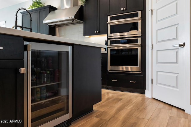2037 E Fallen Leaf Ln, Phoenix, AZ 85024 - kitchen with wall chimney exhaust hood, stainless steel double oven, beverage cooler, light wood-style floors, and light countertops