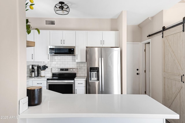 kitchen featuring a barn door, white cabinetry, appliances with stainless steel finishes, and decorative backsplash