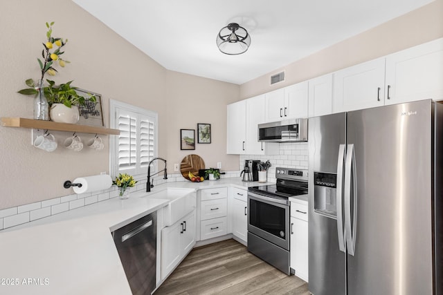 kitchen featuring appliances with stainless steel finishes, white cabinetry, wood-type flooring, sink, and kitchen peninsula