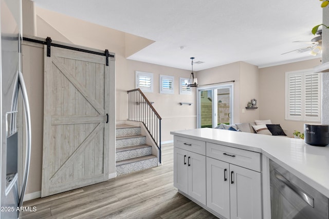 kitchen with hanging light fixtures, stainless steel appliances, a barn door, light hardwood / wood-style floors, and white cabinets