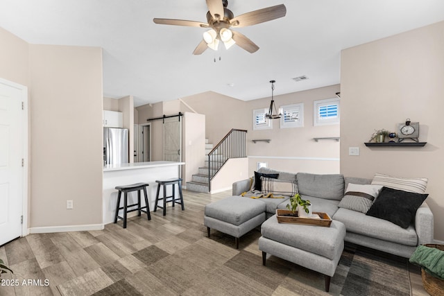 living room with a barn door, light hardwood / wood-style floors, and ceiling fan with notable chandelier