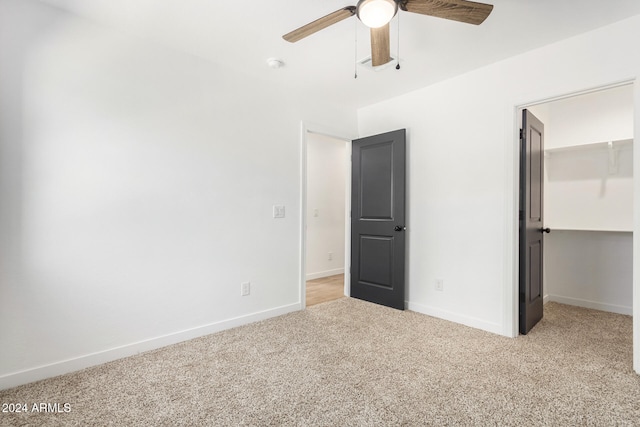 unfurnished bedroom with a spacious closet, light carpet, ceiling fan, and a closet