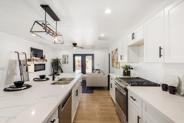 kitchen featuring stainless steel appliances, hanging light fixtures, sink, white cabinets, and light hardwood / wood-style flooring