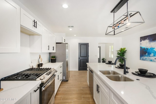 kitchen featuring stainless steel appliances, sink, decorative light fixtures, light hardwood / wood-style flooring, and white cabinets