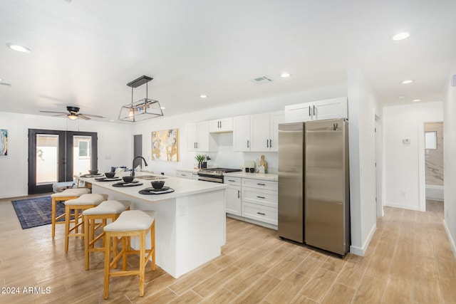 kitchen featuring a center island with sink, stainless steel appliances, light wood-type flooring, white cabinets, and ceiling fan