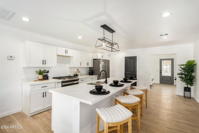 kitchen with stainless steel appliances, white cabinets, sink, a kitchen island with sink, and light hardwood / wood-style flooring