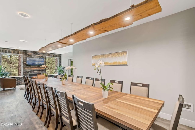 dining room with a fireplace, recessed lighting, brick wall, wood finished floors, and beamed ceiling