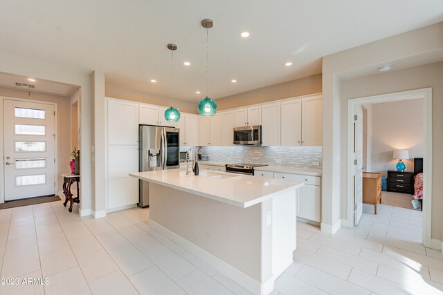 kitchen with an island with sink, white cabinetry, appliances with stainless steel finishes, light tile patterned floors, and decorative light fixtures