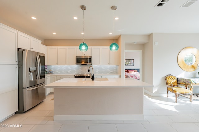 kitchen featuring white cabinets, hanging light fixtures, a center island with sink, backsplash, and appliances with stainless steel finishes