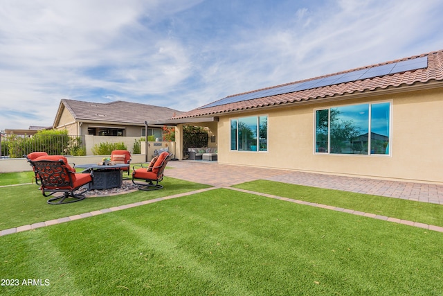 back of property featuring a lawn, solar panels, a patio area, and a fire pit