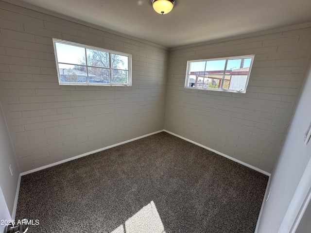 spare room featuring brick wall, plenty of natural light, and carpet