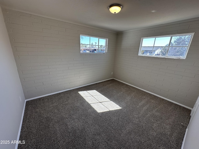 unfurnished room with dark carpet, a wealth of natural light, and brick wall