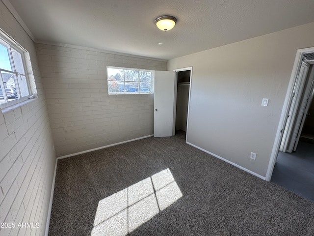 unfurnished bedroom featuring a closet, brick wall, a textured ceiling, and dark colored carpet