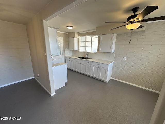 kitchen featuring sink, ceiling fan, white cabinets, and brick wall