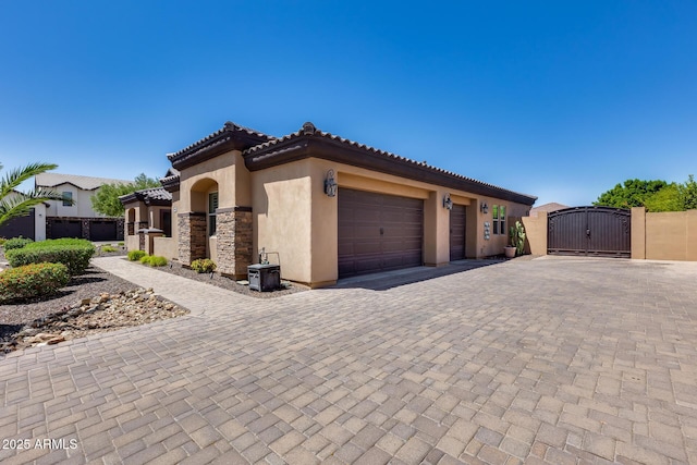 mediterranean / spanish-style home with a garage, stucco siding, a gate, decorative driveway, and a tiled roof