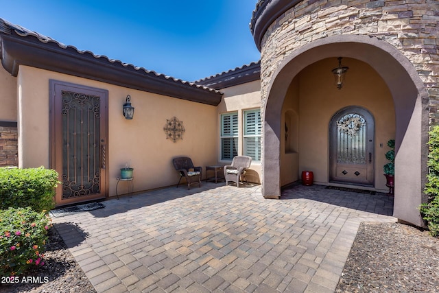 property entrance with stucco siding, a patio area, and stone siding