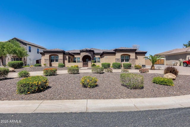 mediterranean / spanish home featuring stucco siding, a tiled roof, and stone siding