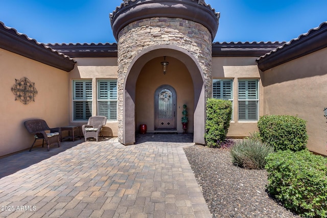 view of exterior entry featuring a patio area, stucco siding, and a tile roof