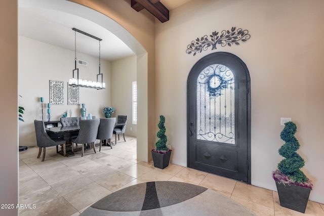 foyer featuring beam ceiling, arched walkways, a chandelier, light tile patterned floors, and visible vents