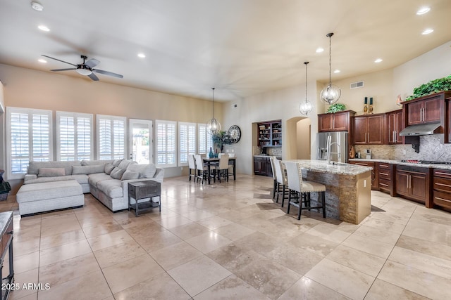 kitchen featuring a breakfast bar area, appliances with stainless steel finishes, tasteful backsplash, ceiling fan with notable chandelier, and under cabinet range hood
