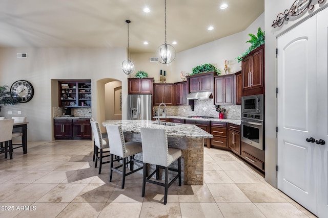 kitchen featuring visible vents, under cabinet range hood, tasteful backsplash, arched walkways, and stainless steel appliances
