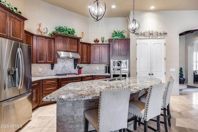 kitchen with a breakfast bar area, arched walkways, stainless steel appliances, tasteful backsplash, and under cabinet range hood