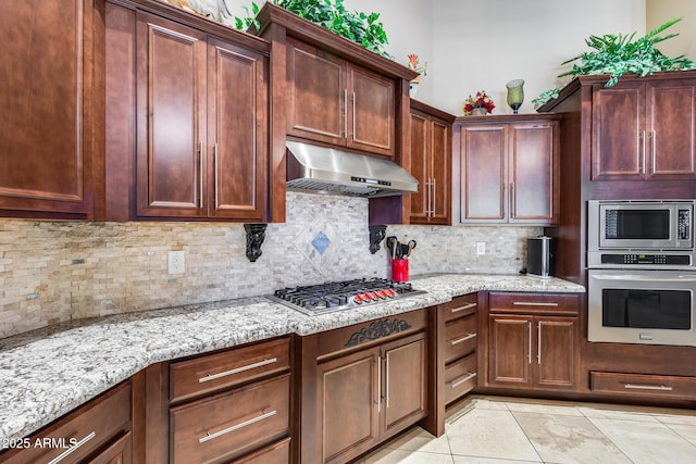 kitchen with tasteful backsplash, light tile patterned floors, light stone counters, under cabinet range hood, and stainless steel appliances
