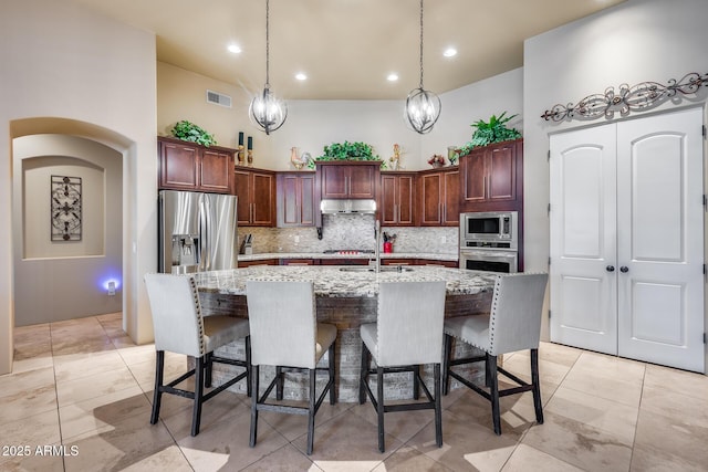 kitchen featuring backsplash, visible vents, under cabinet range hood, a breakfast bar, and stainless steel appliances