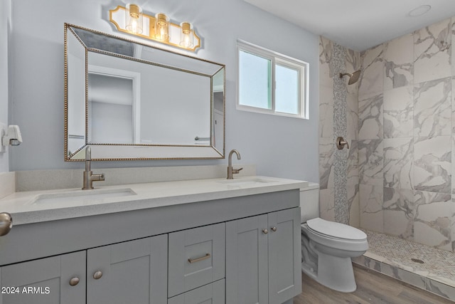 bathroom with hardwood / wood-style flooring, toilet, double vanity, and a tile shower