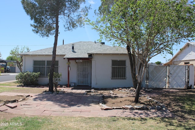 view of front of home featuring stucco siding, roof with shingles, fence, and a gate