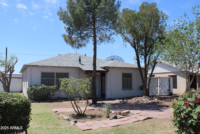 view of front facade featuring a shingled roof, stucco siding, fence, and a front yard