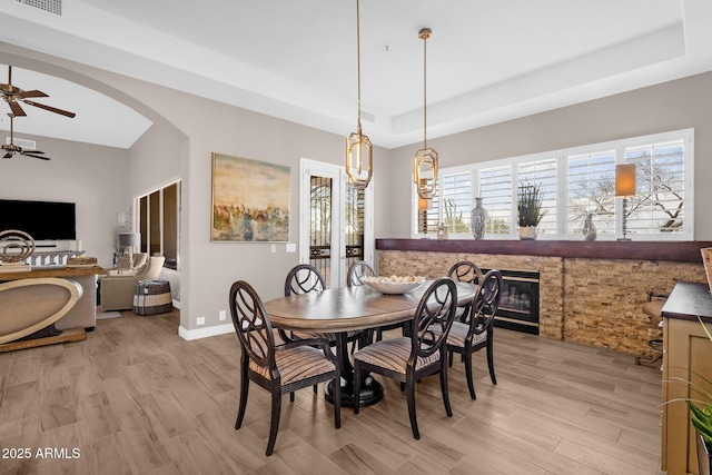 dining area with light wood-type flooring, a tray ceiling, a glass covered fireplace, and arched walkways