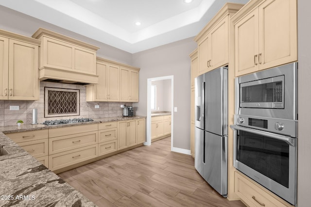 kitchen featuring appliances with stainless steel finishes, a tray ceiling, cream cabinetry, and backsplash