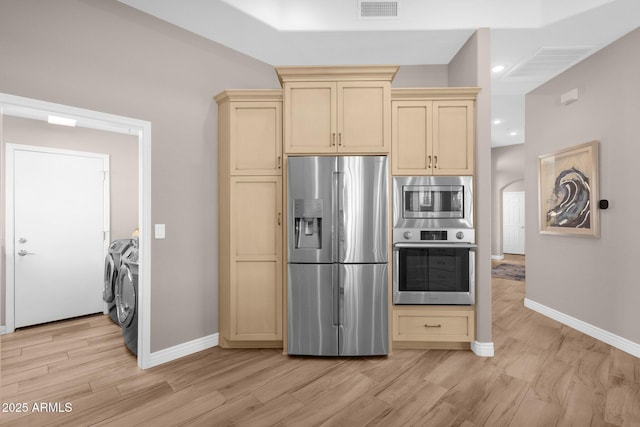 kitchen featuring visible vents, stainless steel appliances, cream cabinetry, and independent washer and dryer