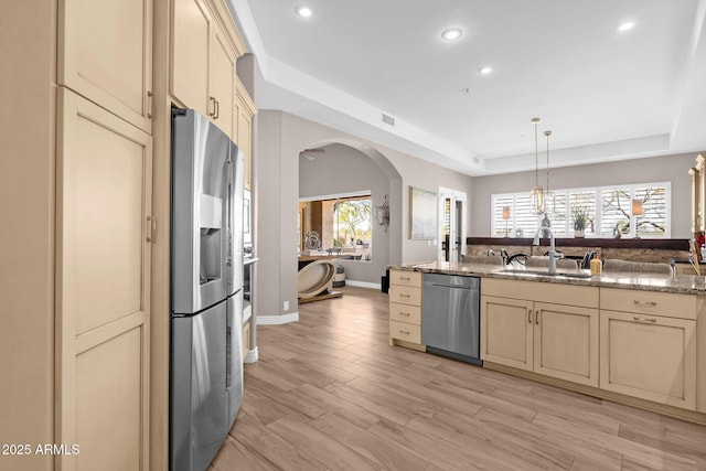 kitchen featuring light wood finished floors, arched walkways, appliances with stainless steel finishes, cream cabinetry, and a sink