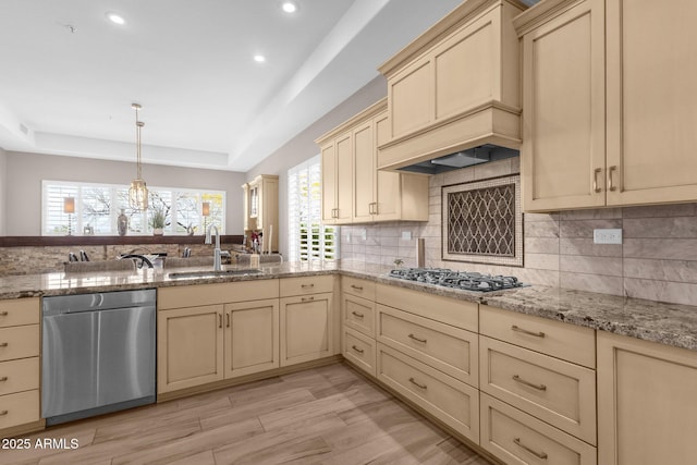 kitchen featuring stainless steel appliances, a sink, cream cabinetry, a tray ceiling, and tasteful backsplash