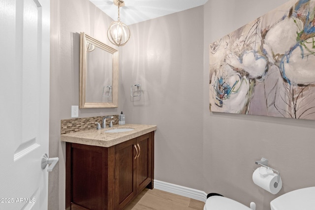 bathroom with decorative backsplash, toilet, vanity, a chandelier, and baseboards