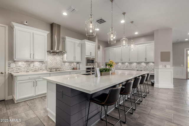 kitchen with wall chimney range hood, white cabinets, a large island, and stainless steel microwave