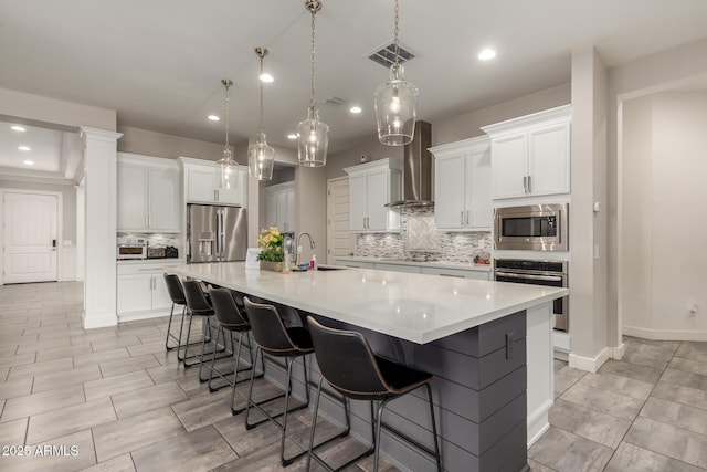 kitchen featuring a spacious island, wall chimney range hood, appliances with stainless steel finishes, and white cabinets