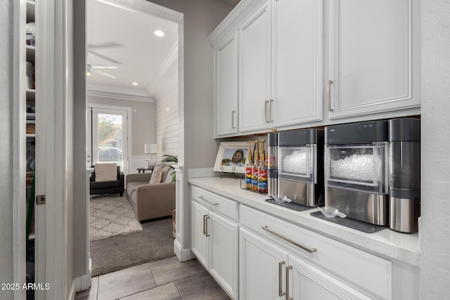 bar featuring ceiling fan, light colored carpet, white cabinetry, light stone counters, and ornamental molding